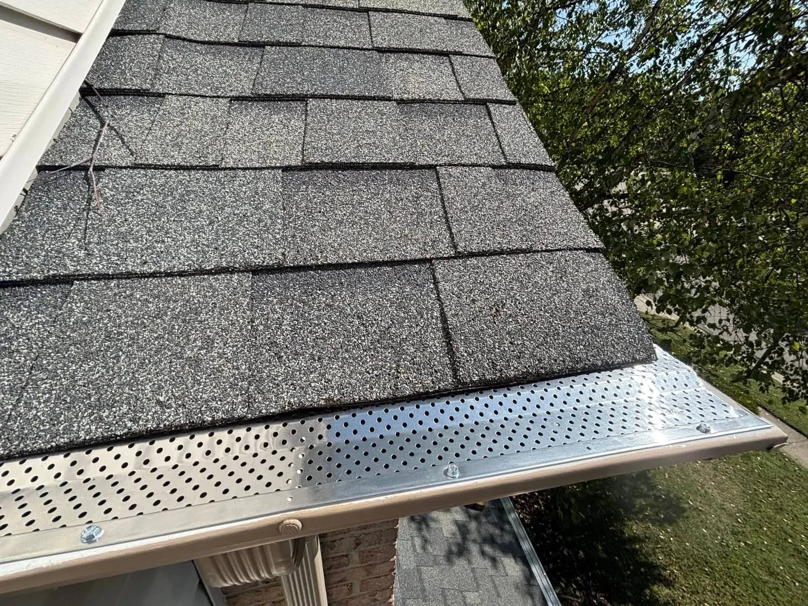 New shingles at the roof edge above a gutter with a guard